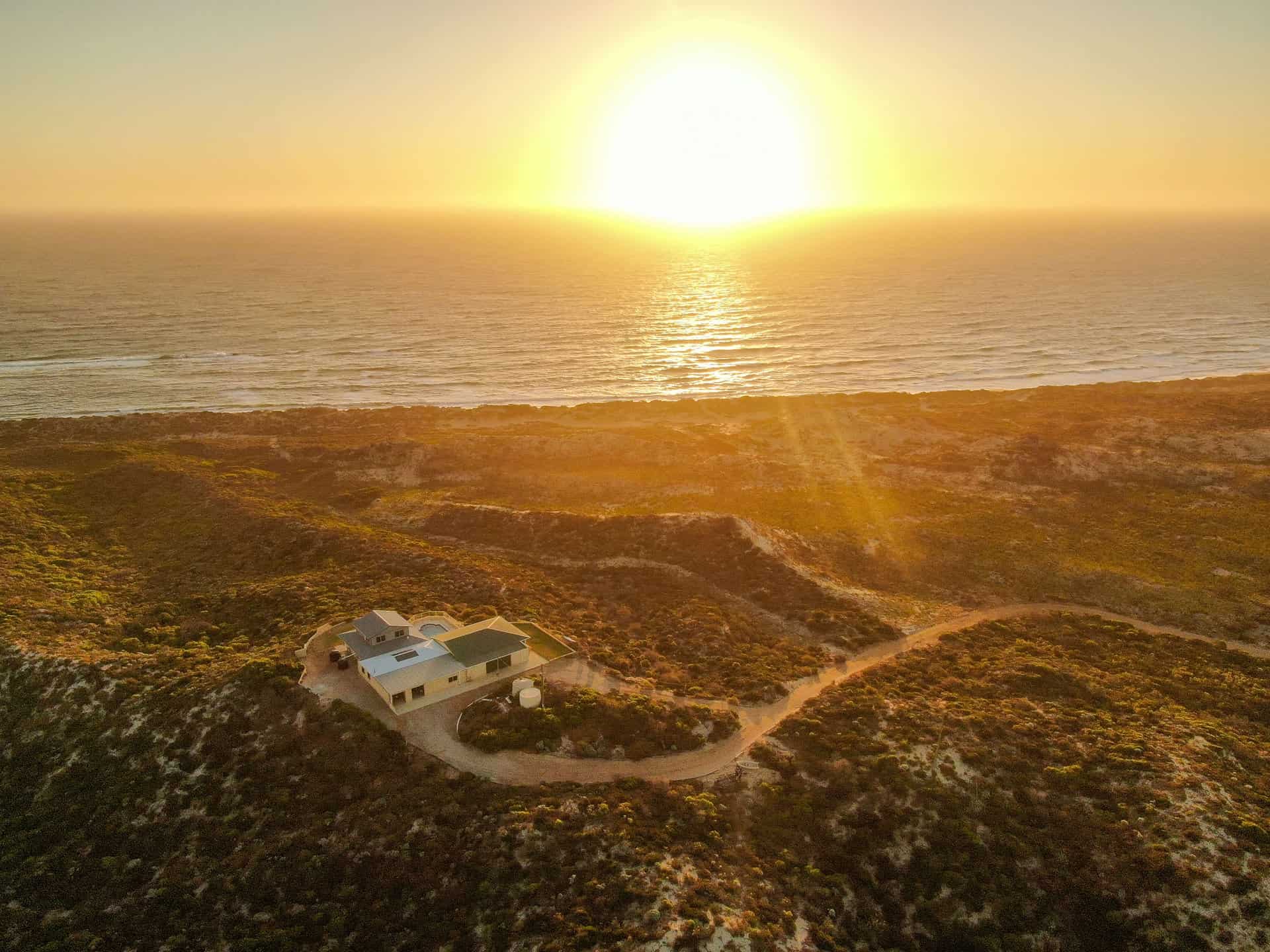 Aerial drone shot overlooking The Glass House WA, the sand dunes and a sunset in Western Australia